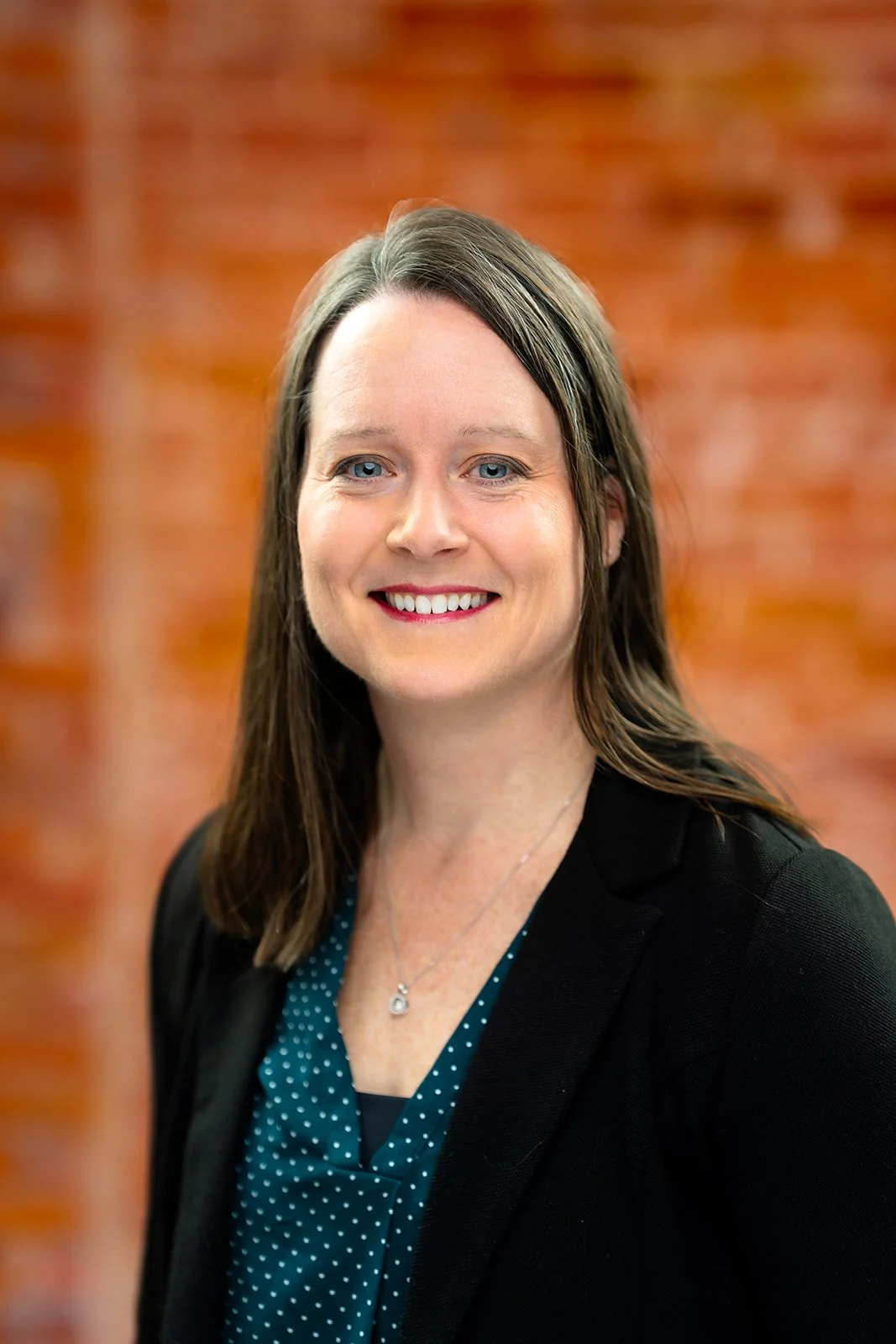 photo of a smiling businesswoman posing for a studio headshot with red brick background