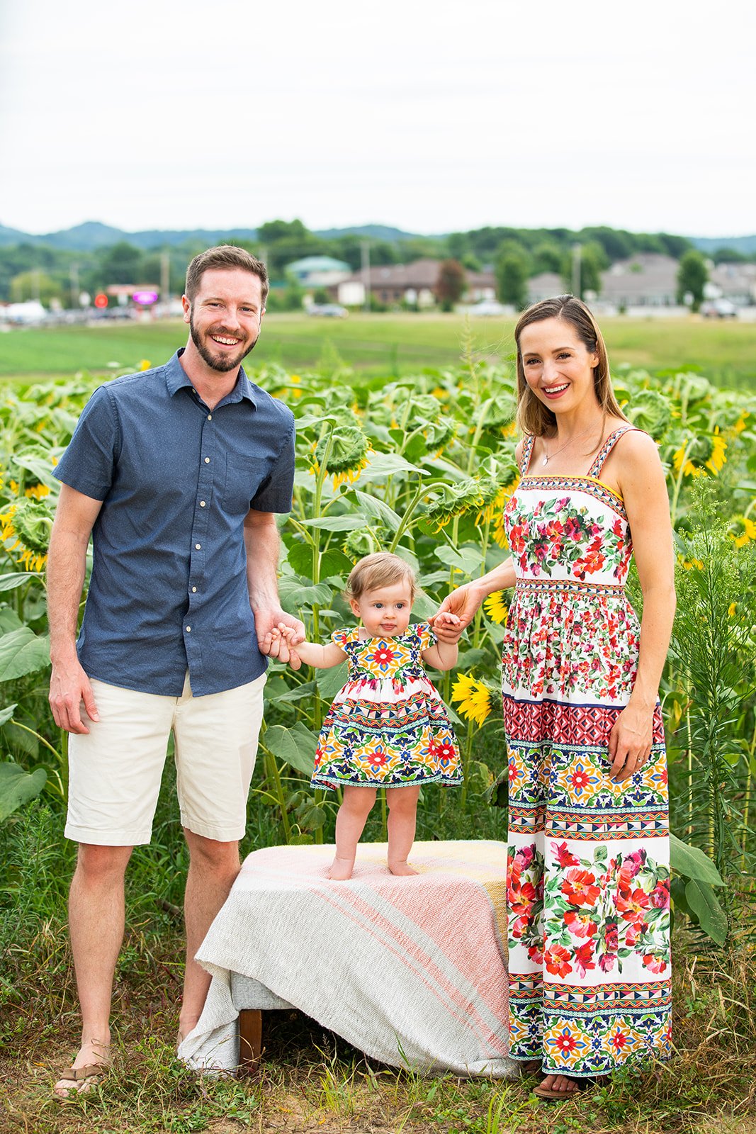 a family of three pose in a sunflower garden