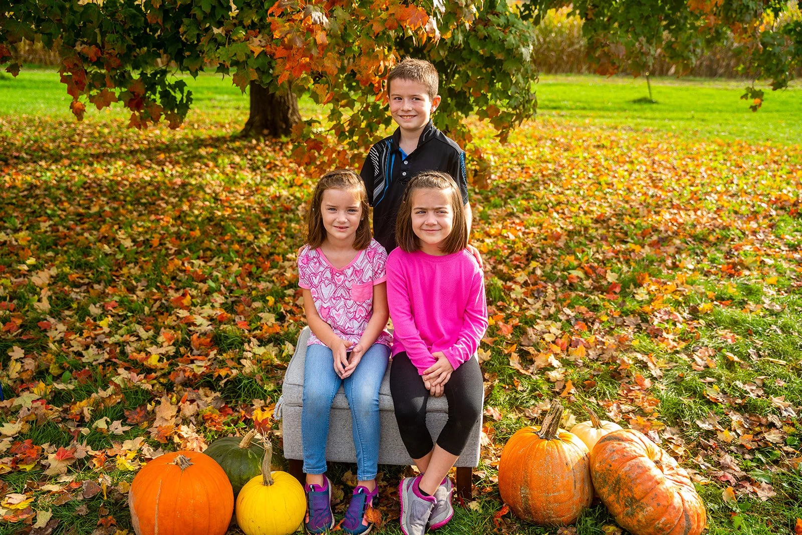 three kids smile for a family picture in the fall next to pumpkins