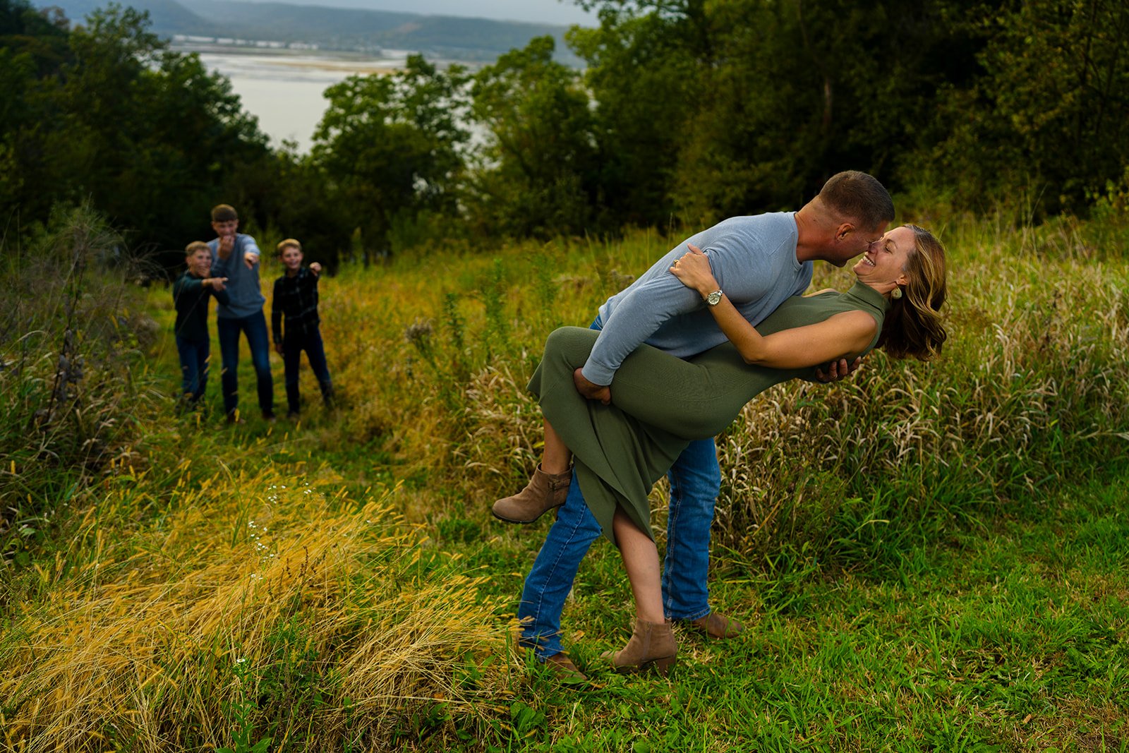 a husband dips and kisses wife as their children cover their eyes