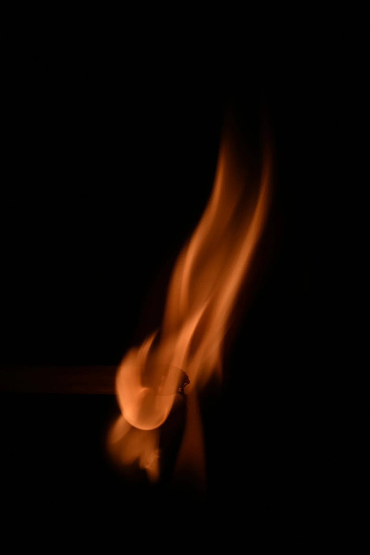Close-up of a lit matchstick with a glowing flame against a black background.