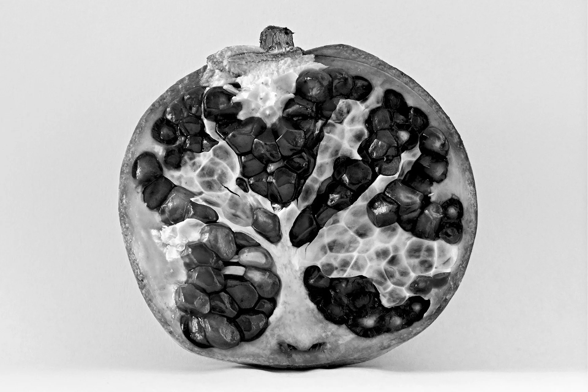 Black and white close-up image of a pomegranate fruit cut in half, showing seeds and inner flesh.