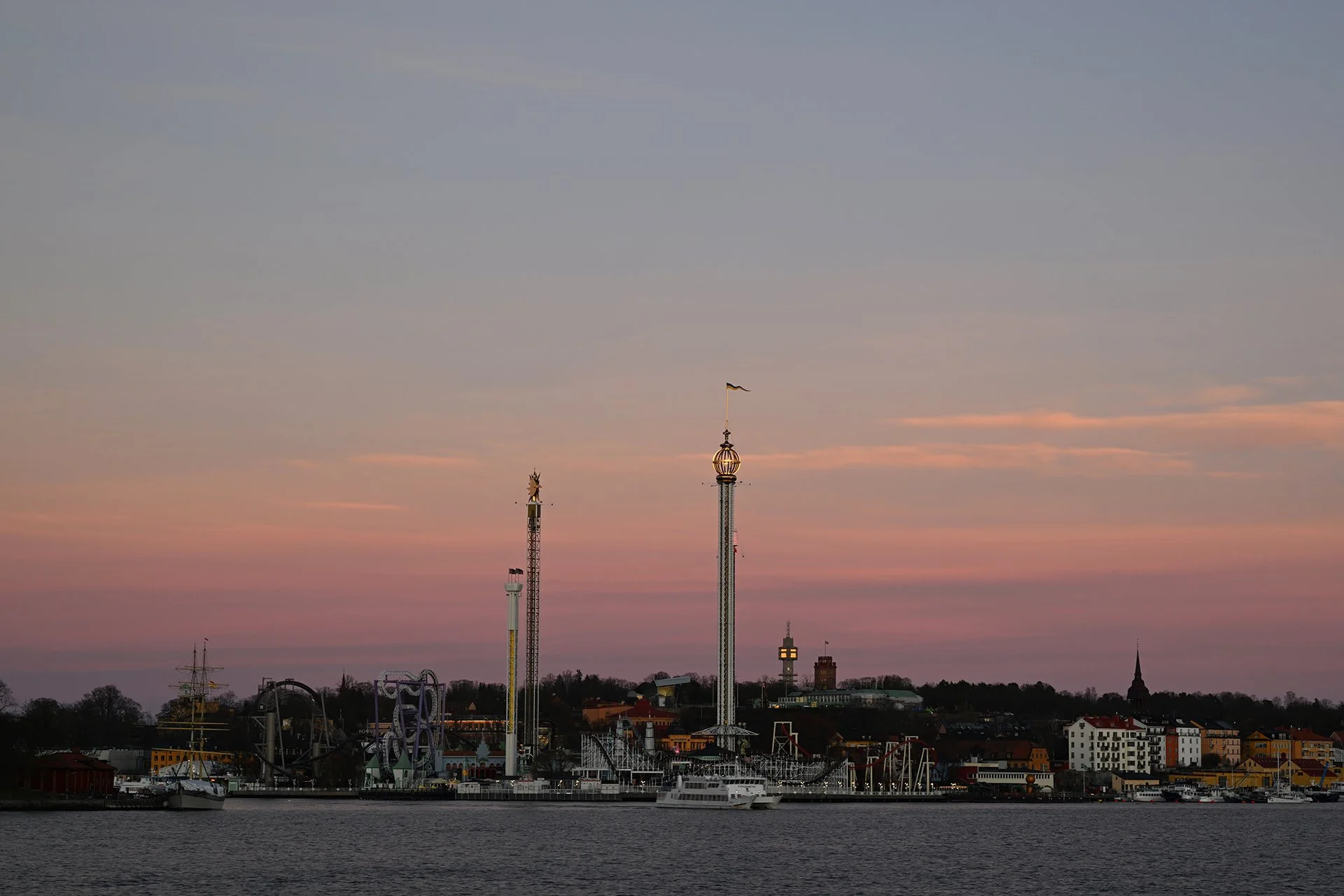 Skyline of a coastal amusement park at sunset with rides and buildings.