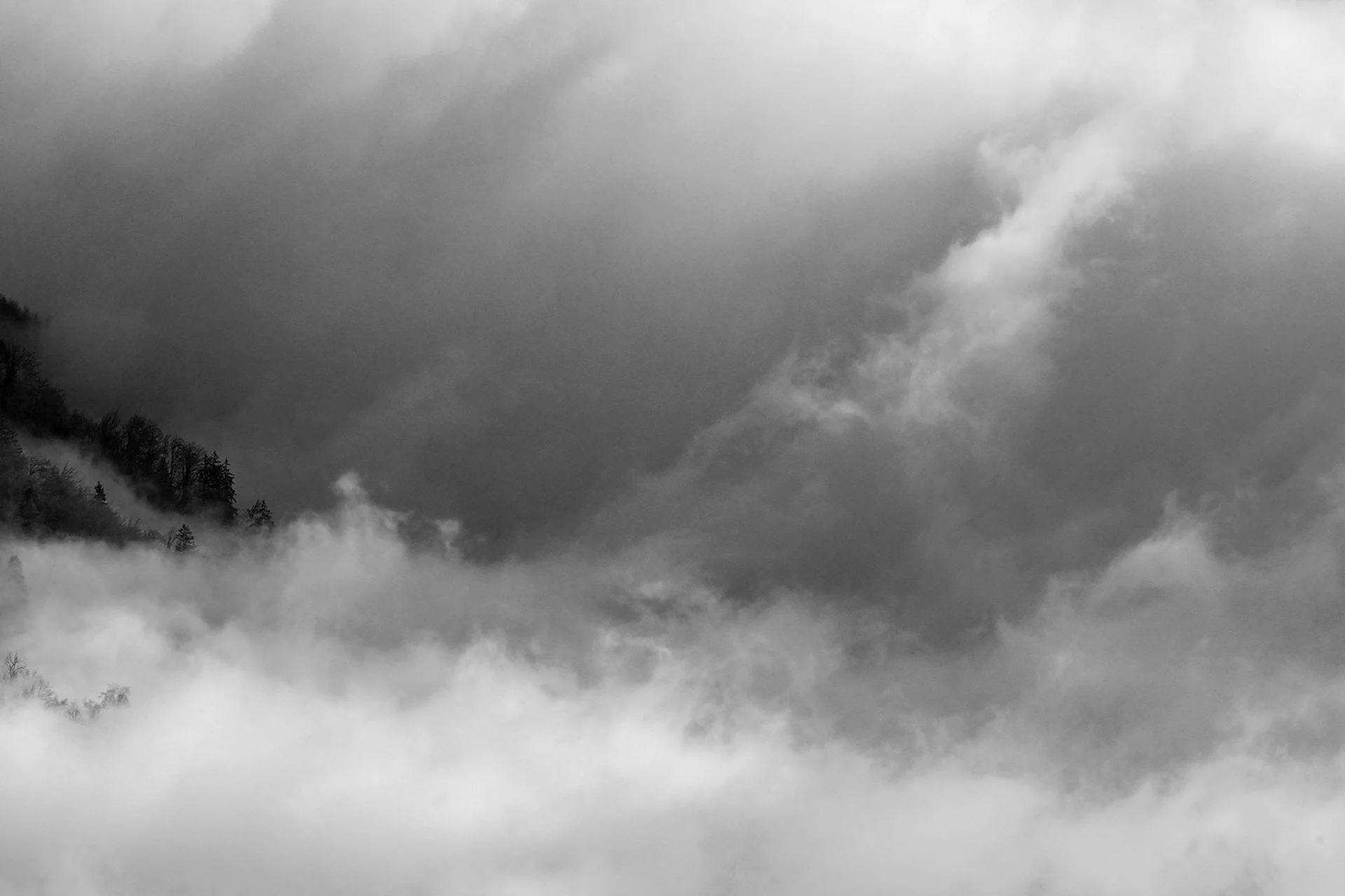 Black and white photo of misty mountains with fog and clouds.