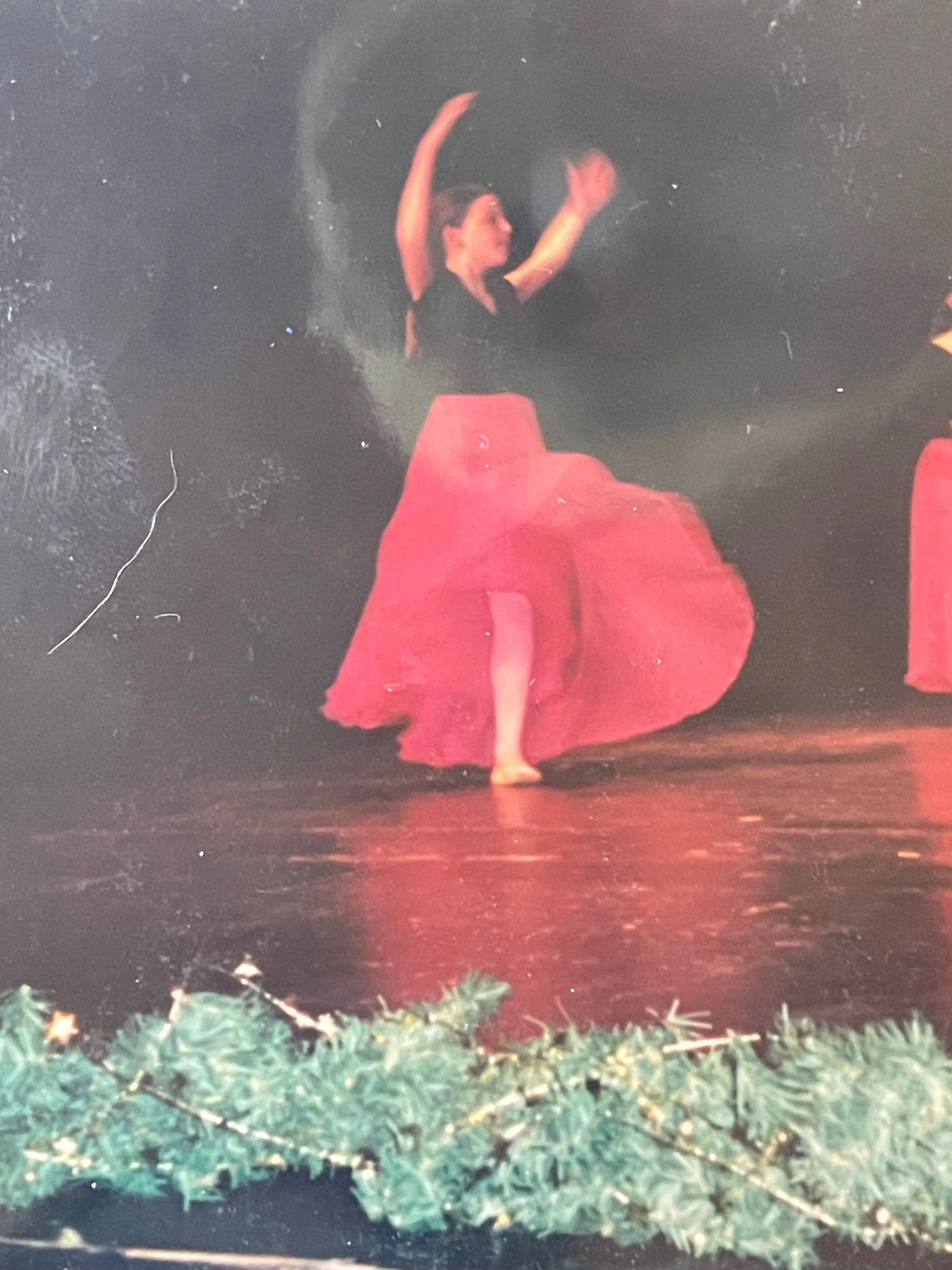 A woman dancing on stage wearing a red skirt and a black top, with festive decorations at the front of the stage.