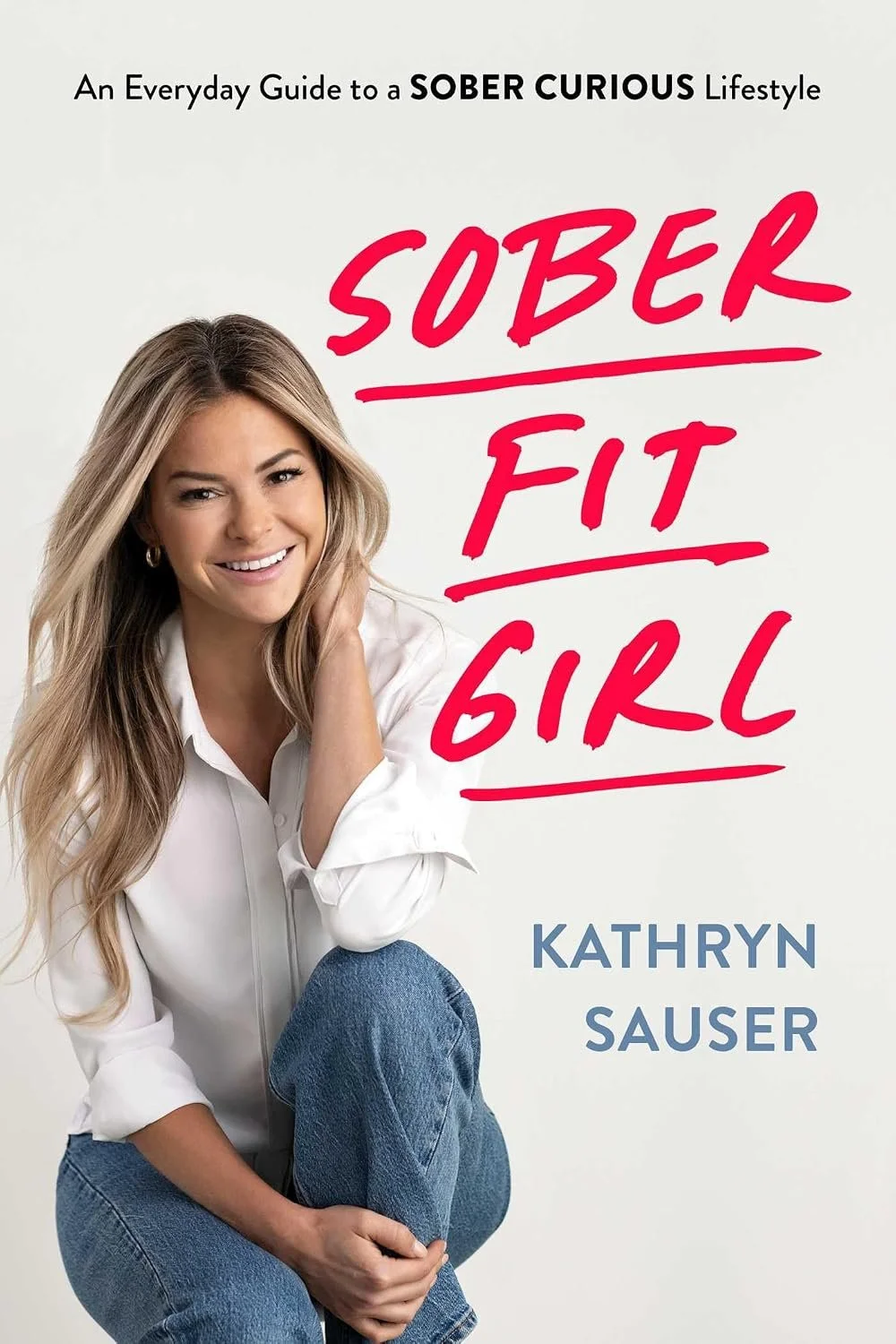 Book cover of Sober Fit Girl by Kathryn Sauser, featuring the smiling author seated in a white shirt and jeans beside the title in bright pink lettering.