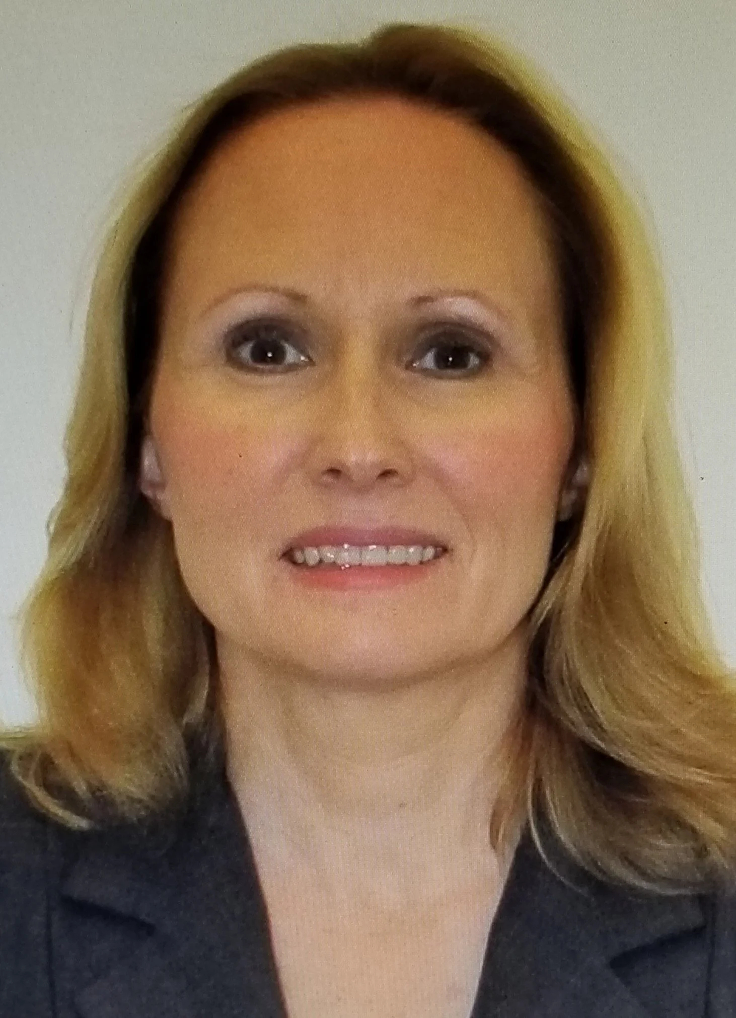 Close-up of woman with blonde hair wearing black top, smiling, with a white background.