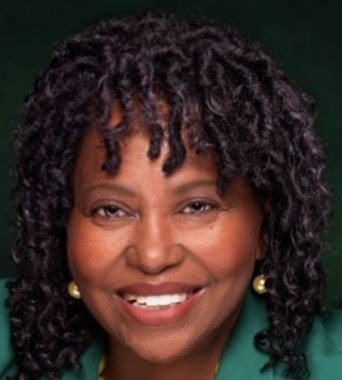 Close-up of a smiling woman with curly black hair, wearing pearl earrings and a green top.