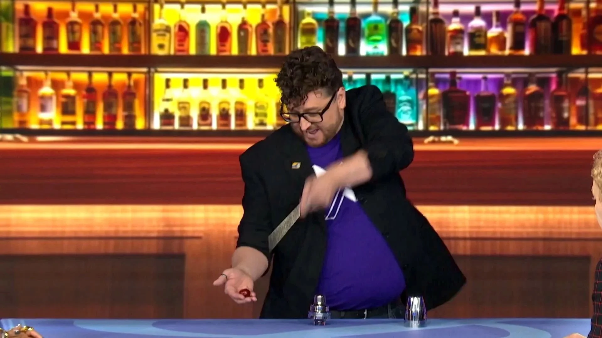 Glenn West mid performance on Fool Us, pointing a wand at a cherry in his hand.