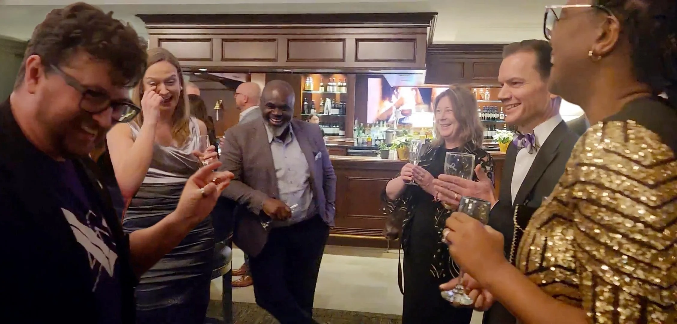 Group of diverse people at a social gathering, smiling and holding glasses, in a bar or restaurant setting.