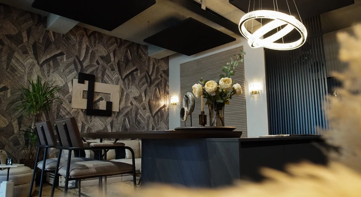 Modern interior with a round light fixture, a wall with leaf-patterned wallpaper, a large table with a vase of white roses, and black decorative wall art.