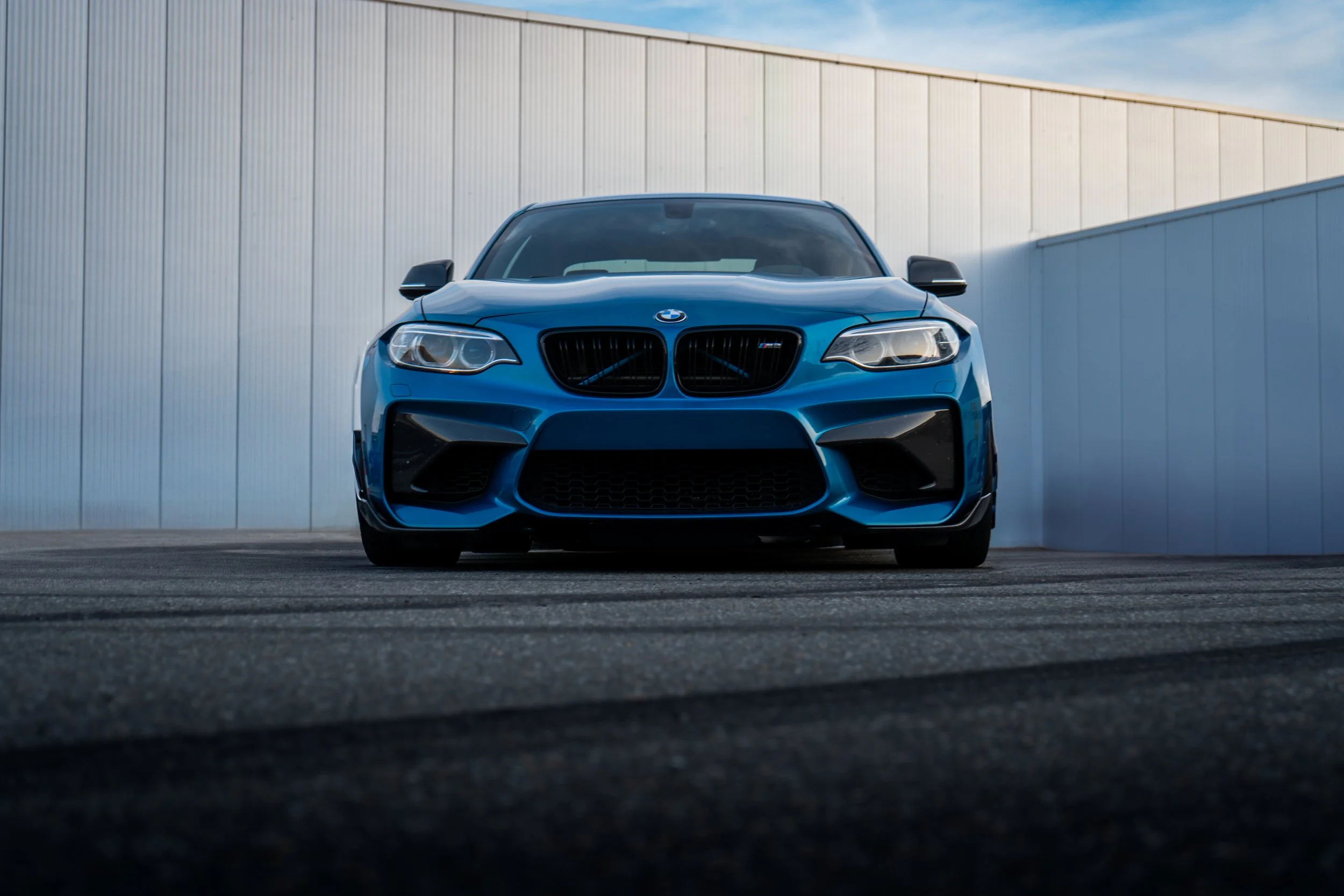 A blue sports sedan parked in front of a large metallic building during daytime.