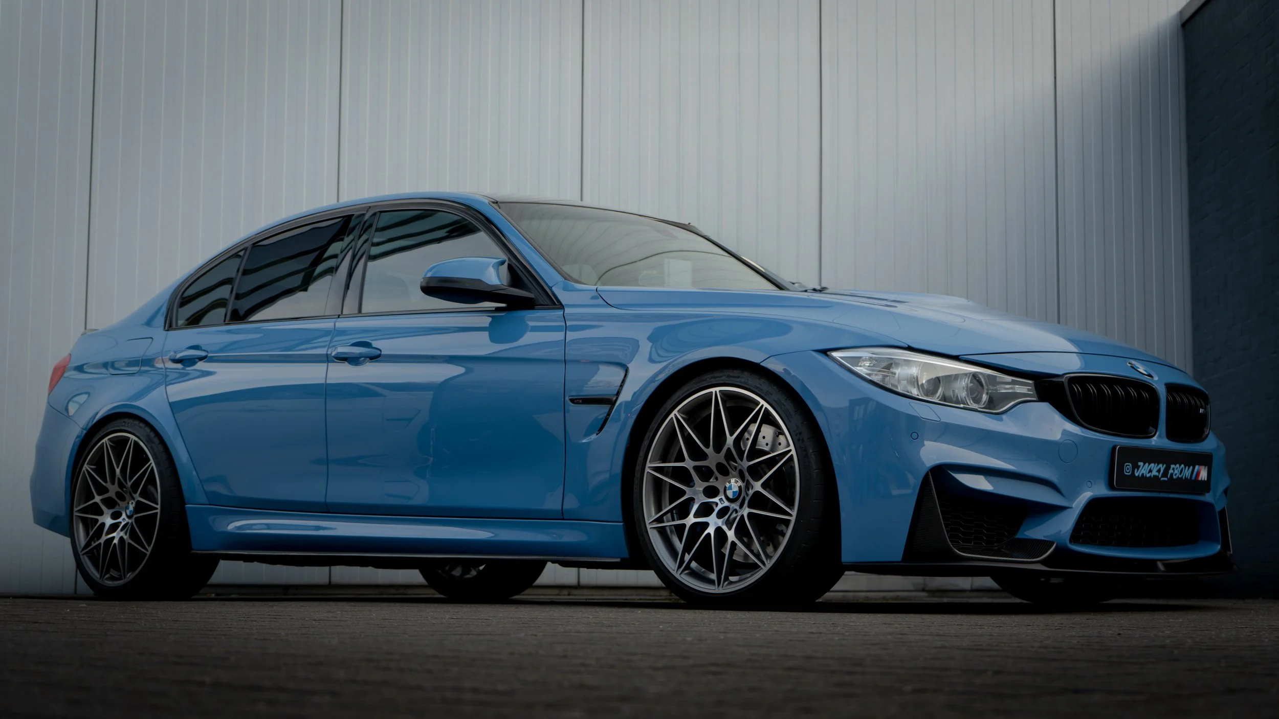 A blue BMW sedan parked near a gray metal wall.
