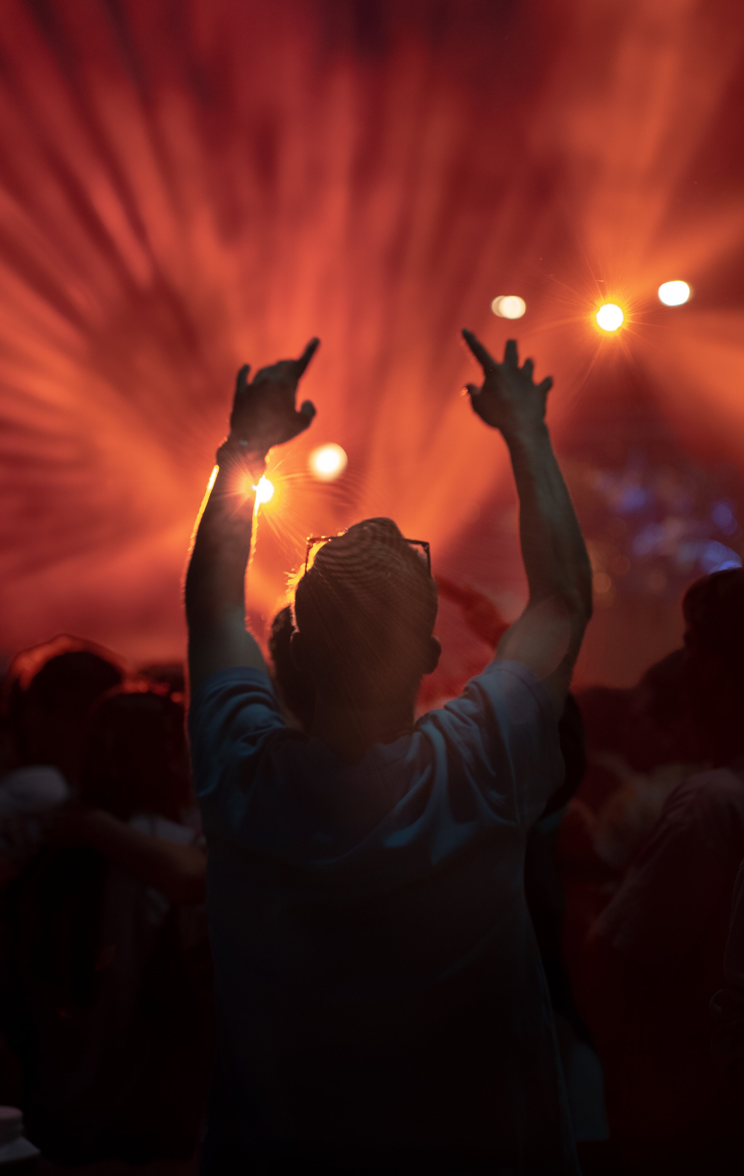 Person at a concert or festival with arms raised against a background of colorful stage lights and other people.