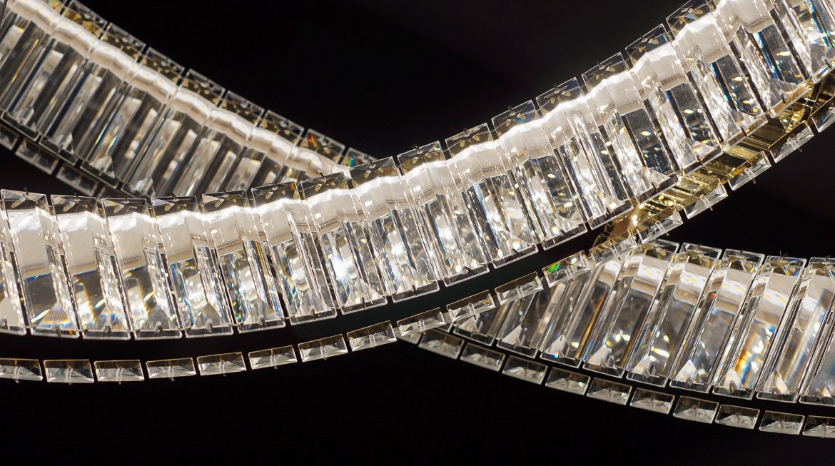 Close-up view of a sparkling, modern crystal chandelier with rectangular glass pieces reflecting light against a dark background.