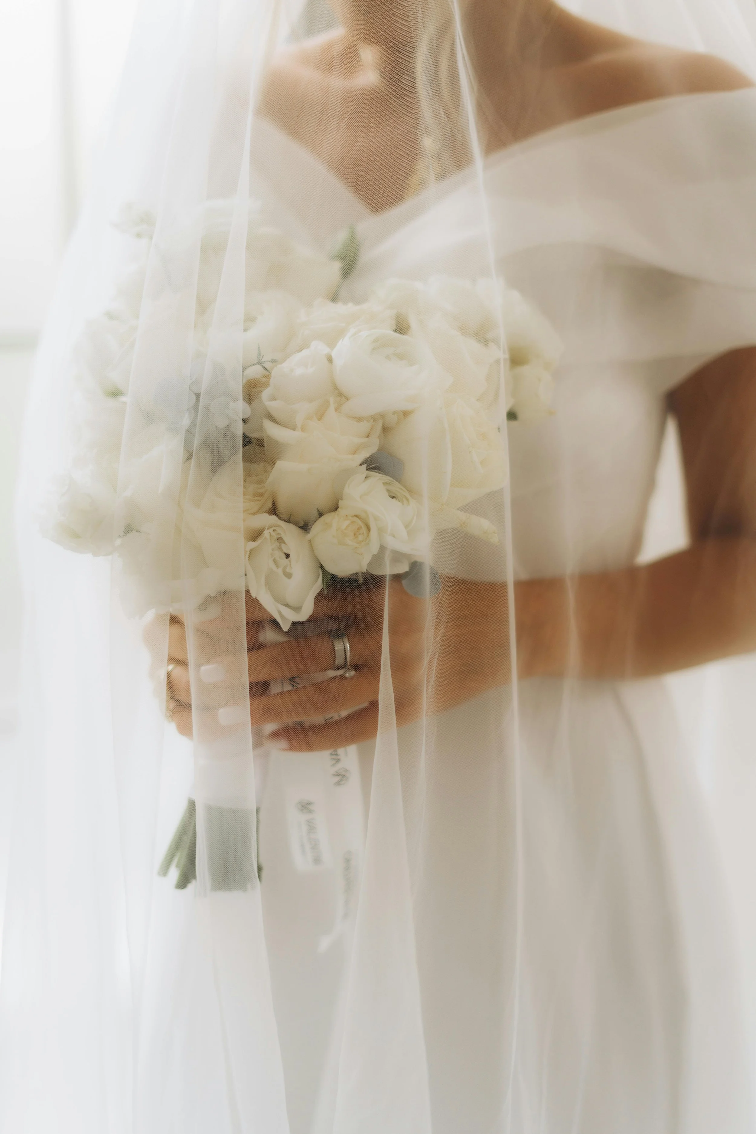 Bride holding a bouquet of white flowers, covered slightly by a sheer white veil.