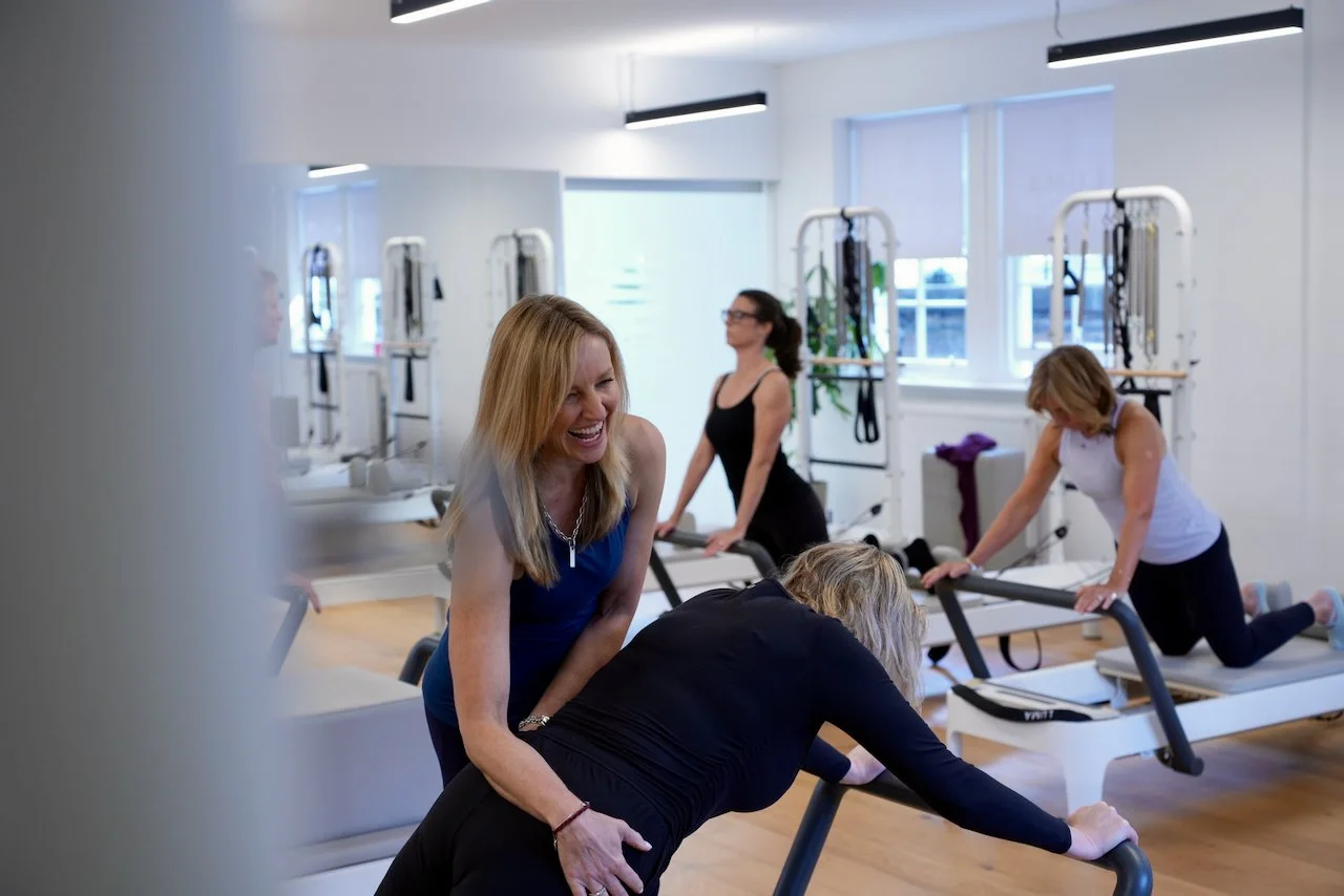 Lucia Poulter cueing a client during a Reformer Pilates class at Luma Pilates Edinburgh, with other women working on Reformers in the background