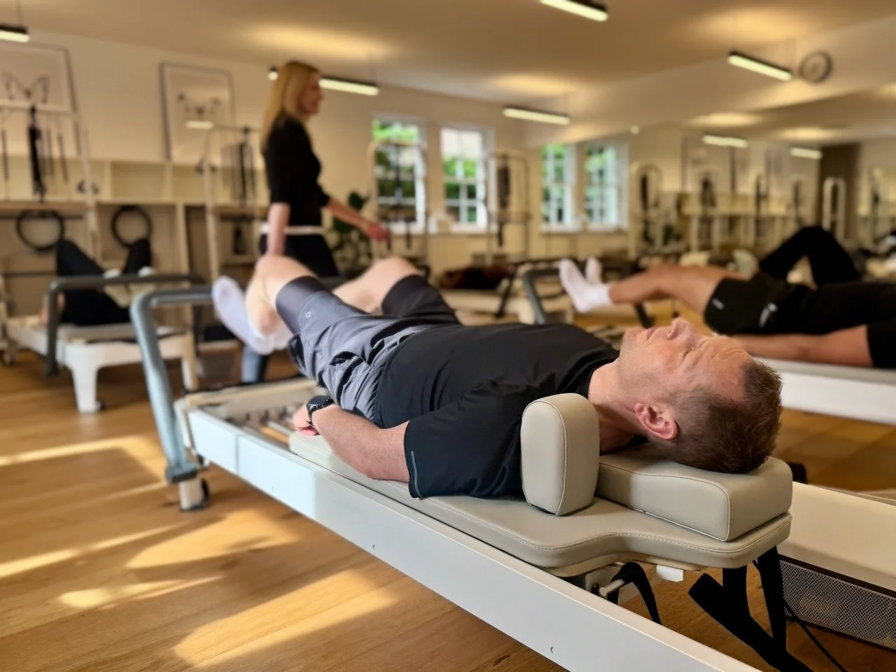 Clients lying on Reformers during a group class at Luma Pilates Edinburgh with Lucia Poulter cueing in the background