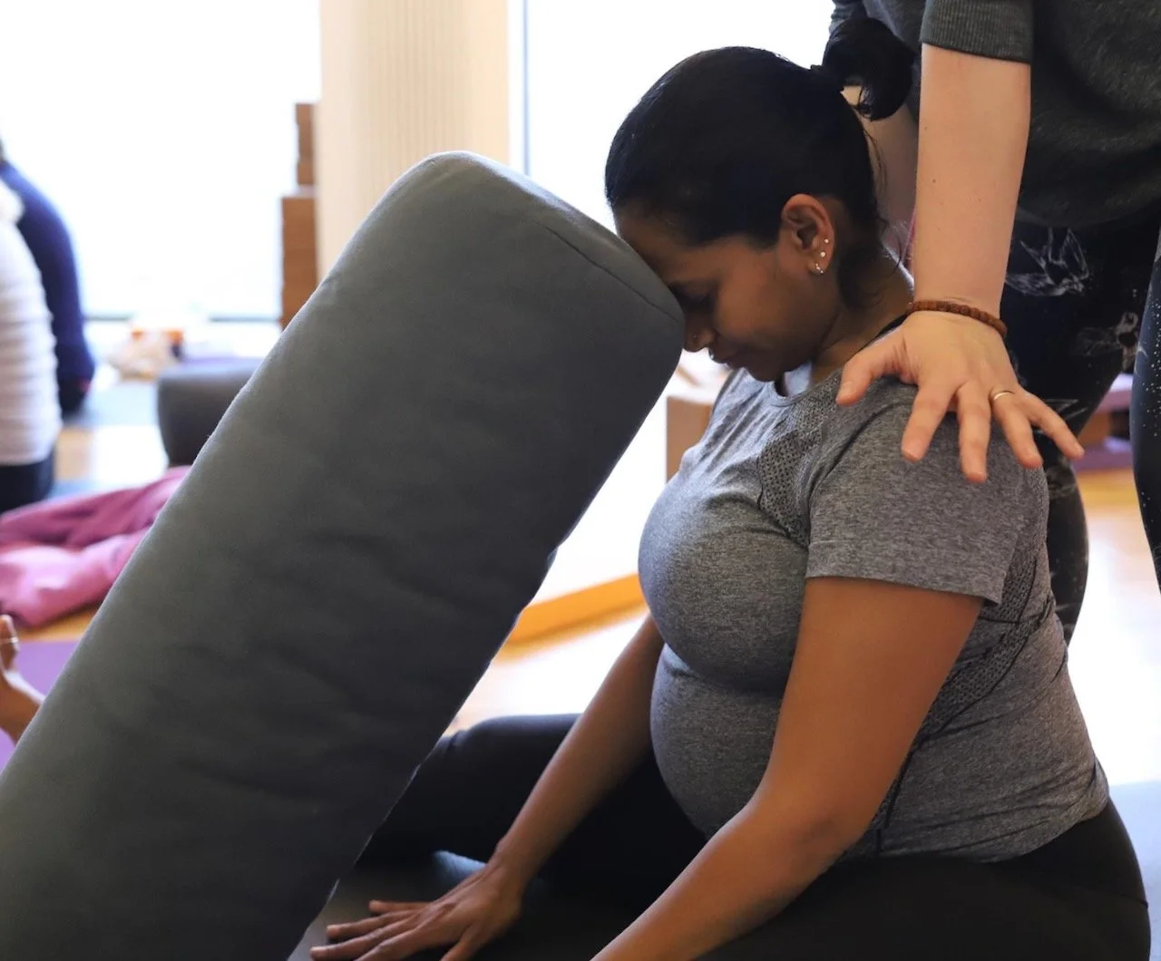 Kat Aydin making a hands-on adjustment with a third trimester client using a bolster during a prenatal Yoga class