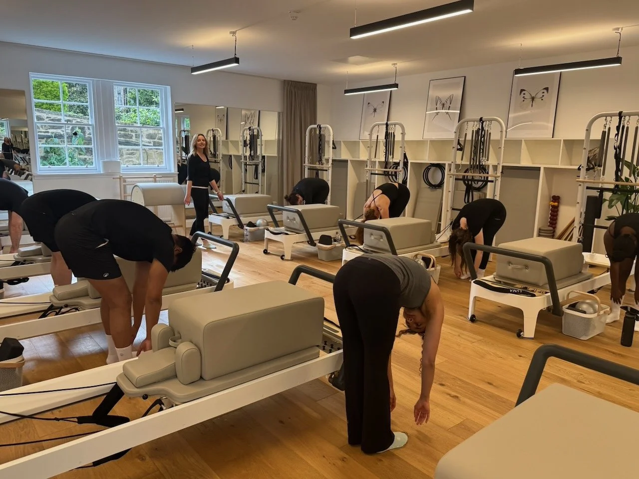 Lucia Poulter overseeing clients performing a roll down beside their Reformers during a group class in Studio A at Luma Pilates Edinburgh