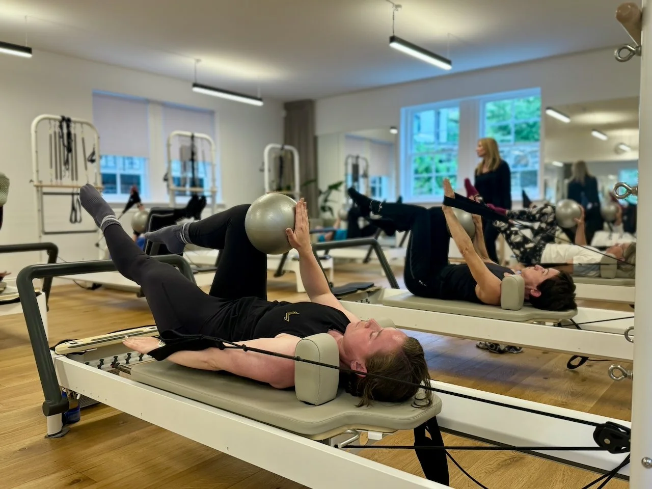 Clients working through low-load abdominal exercises on the Reformer at Luma Pilates, Edinburgh, with instructor Lucia Poulter visible in the background