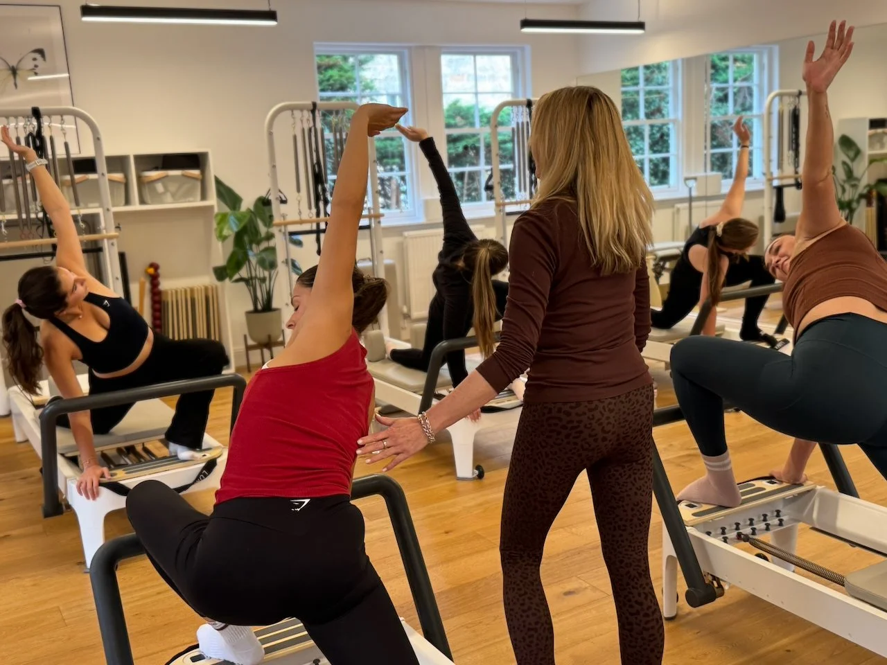 Lucia Poulter cueing a client's oblique during a group side-stretch exercise on the Reformer
