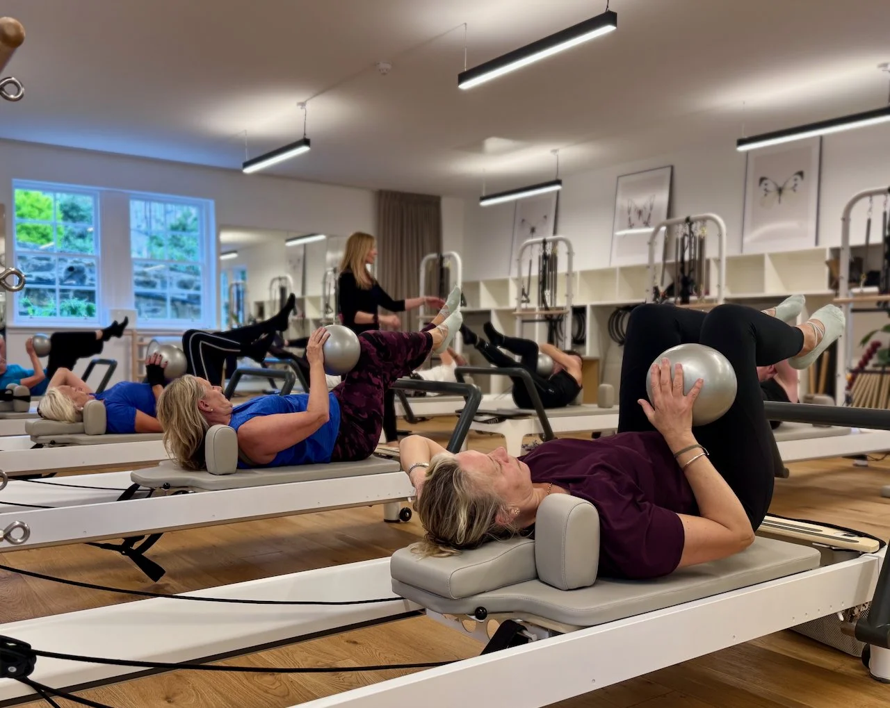 Women performing ball work in a group Reformer Pilates class at Luma Pilates Edinburgh, with Lucia Poulter cueing in the background