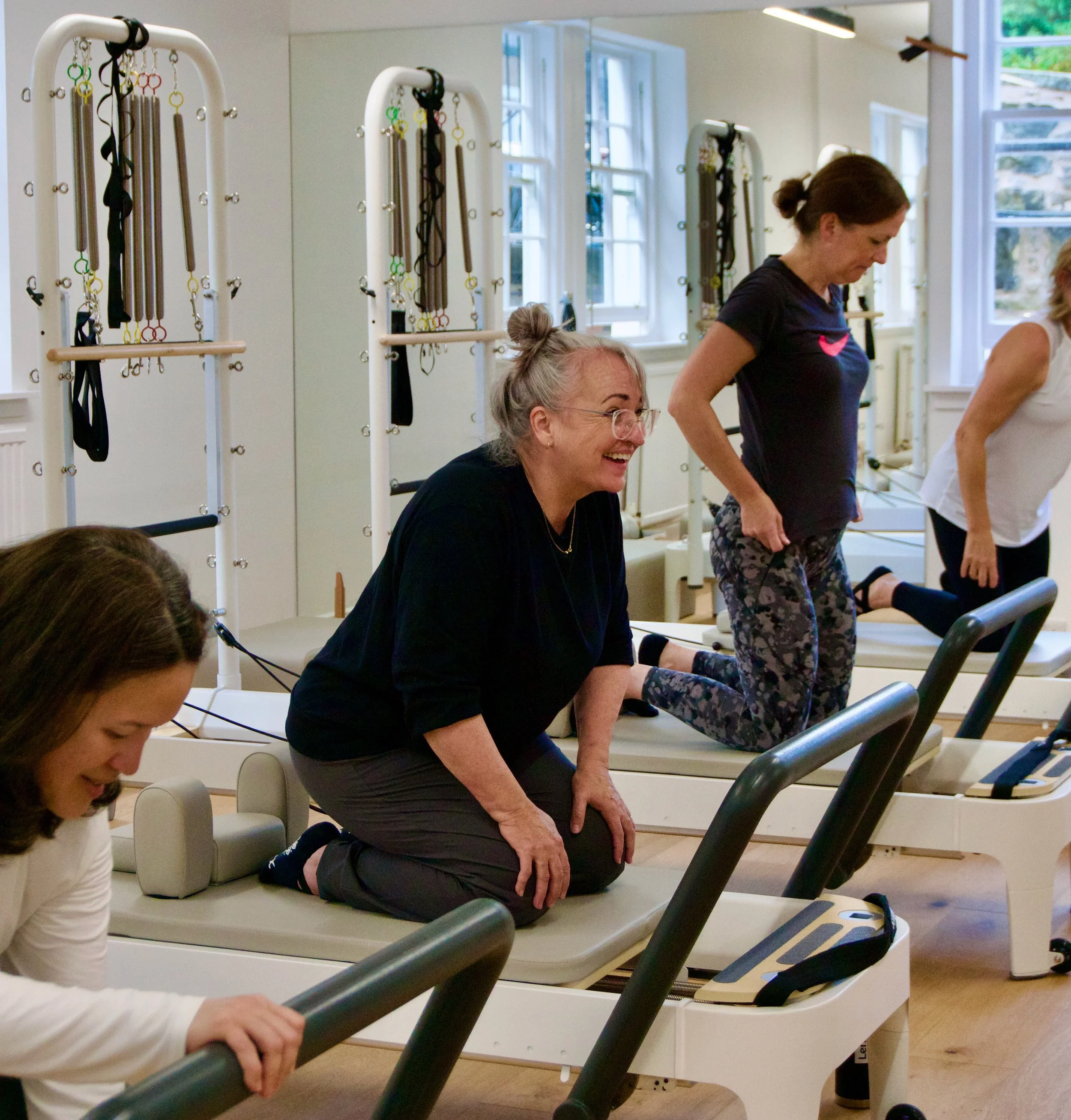 Women doing Pilates exercises on reformer machines in a bright fitness studio.