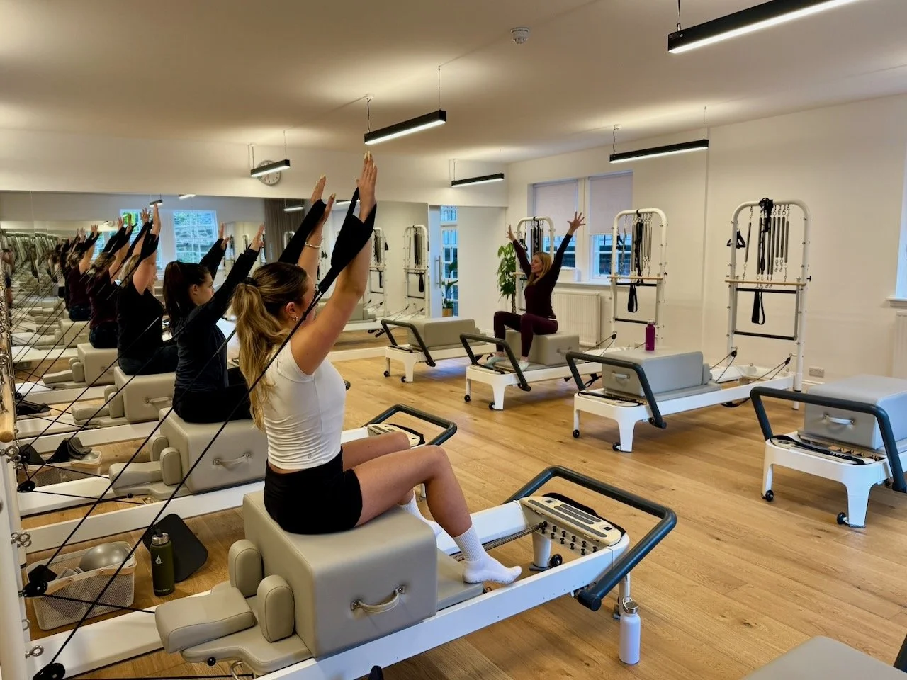 A Reformer Pilates class at Luma Pilates in Edinburgh, clients seated on Reformers with arms raised in a spinal extension sequence