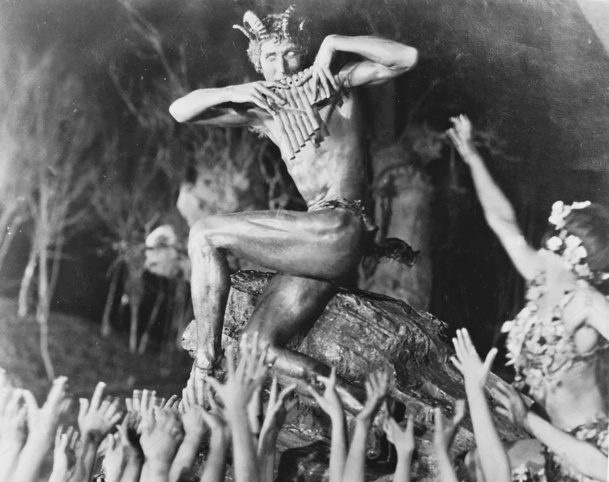 Une photo en noir et blanc d'une personne assise jouant d'un instrument à vent en os, probablement une flûte, entourée de végétation.