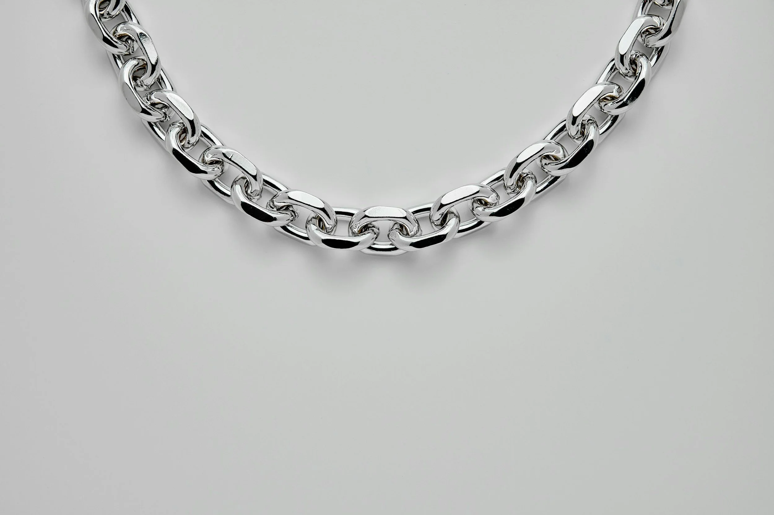 Close-up of a silver chain necklace with large interlocking links, resting on a plain light gray background.
