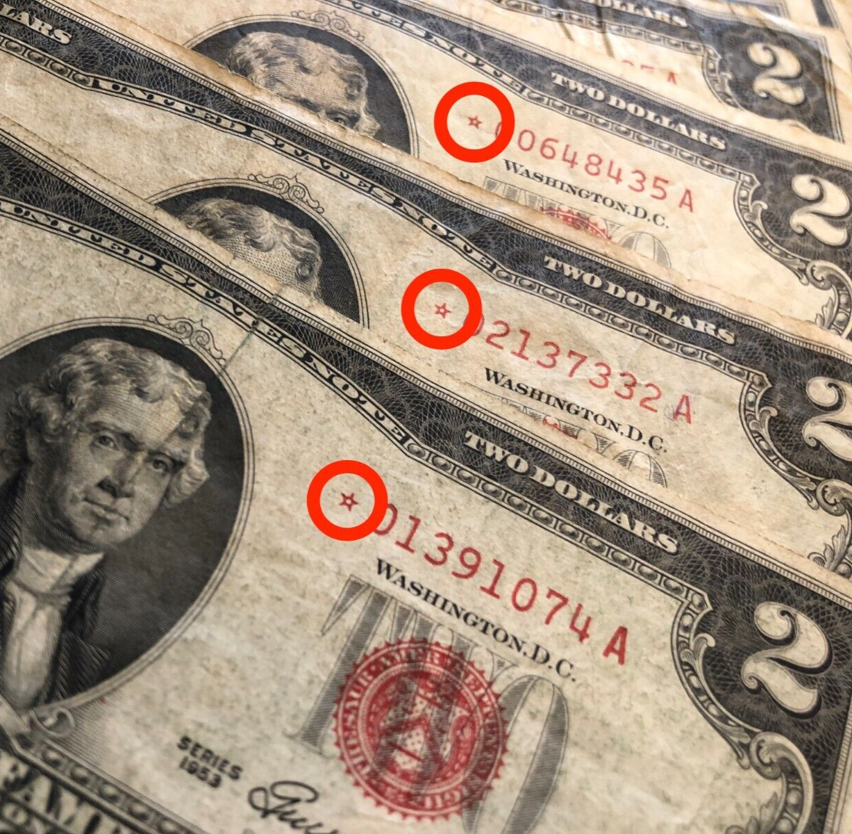 Close-up of three two-dollar bills with red circles highlighting their serial numbers.