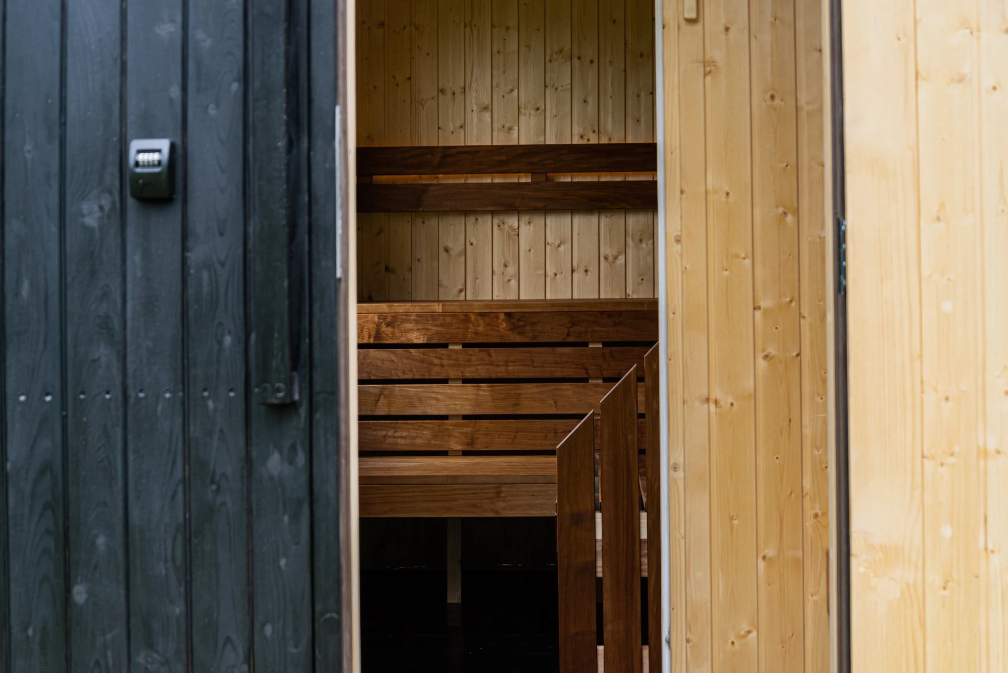 Inside a sauna, with wooden benches and walls, partly viewed through an open door.