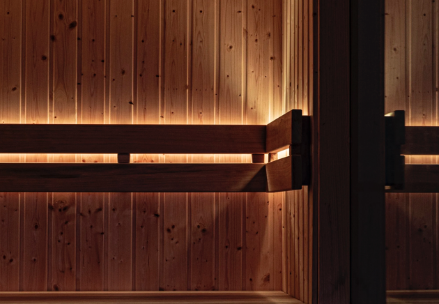 Inside Other Fold Sauna wooden sauna with horizontal wooden benches and vertical wooden walls illuminated by soft lighting.