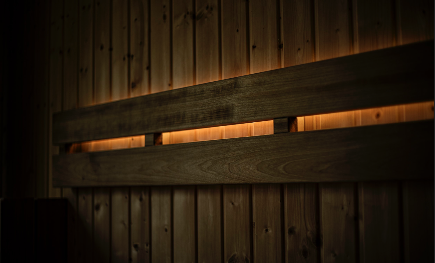 Close-up of a wooden headboard with warm backlighting on a wooden wall.