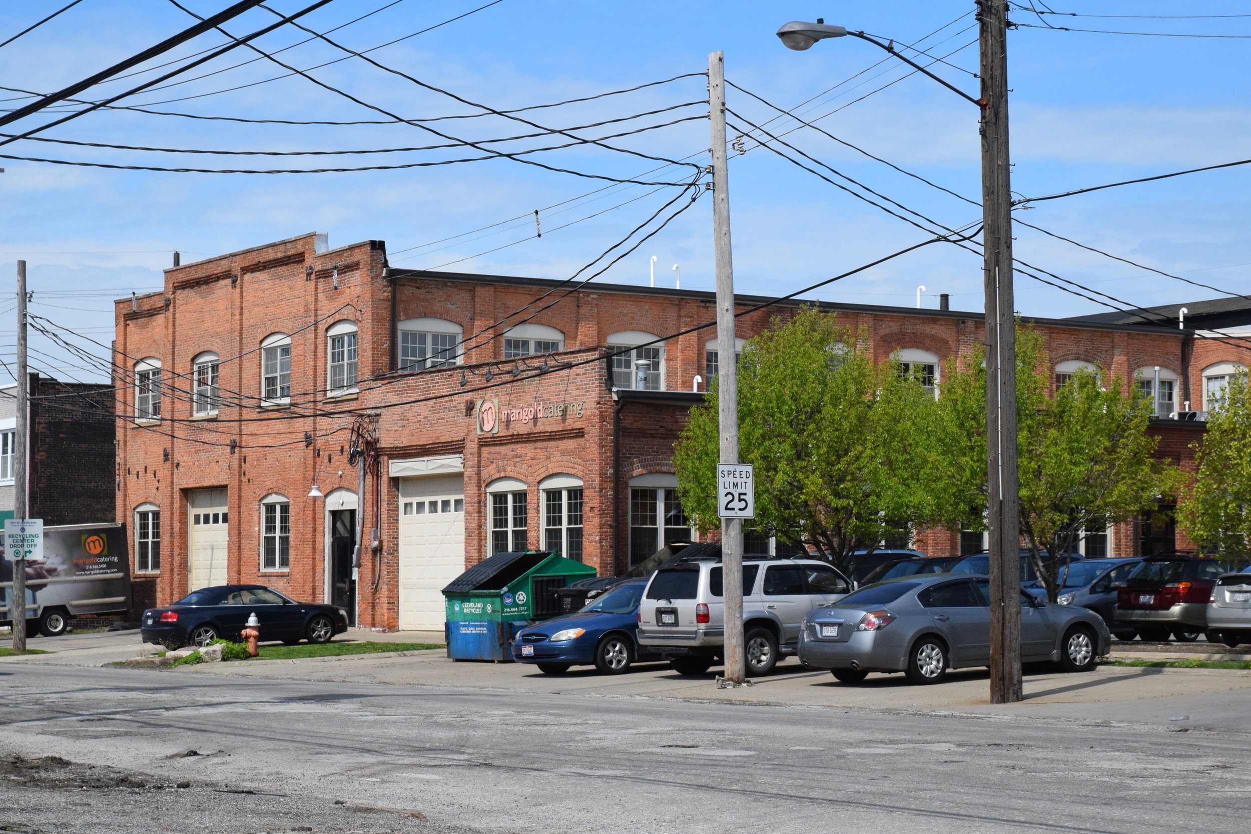 A brick building with multiple windows, parked cars, utility poles, and a street with a 25 mph speed limit sign.