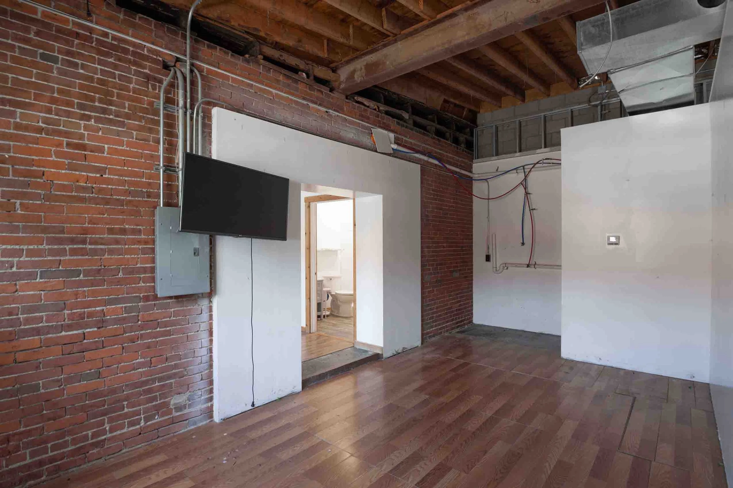 Empty room with exposed brick walls, wooden beams, and a flat-screen TV mounted on the wall.