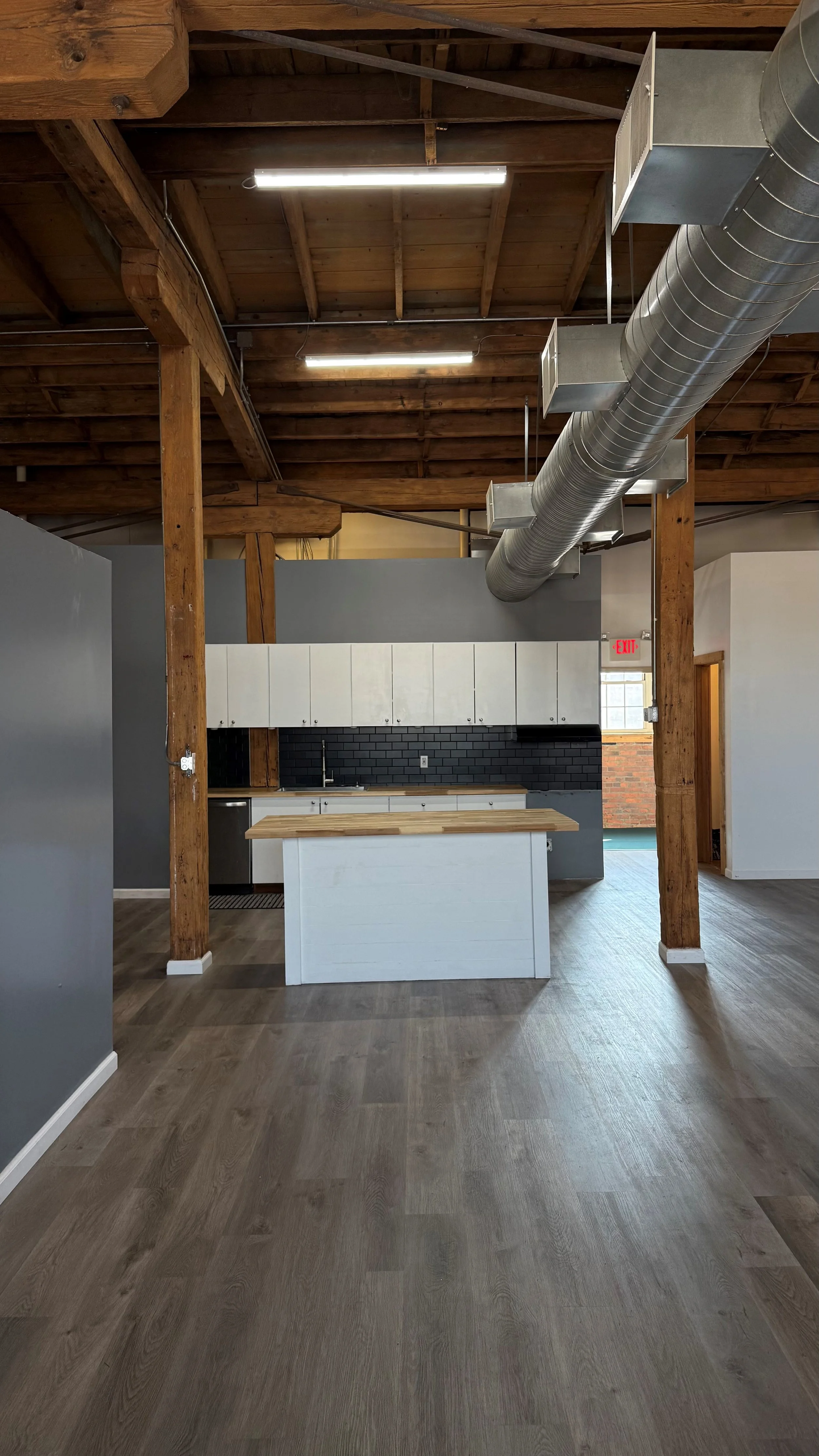 Modern open-concept kitchen with wooden beams, white cabinetry, black subway tile backsplash, and a central island with a wooden countertop.