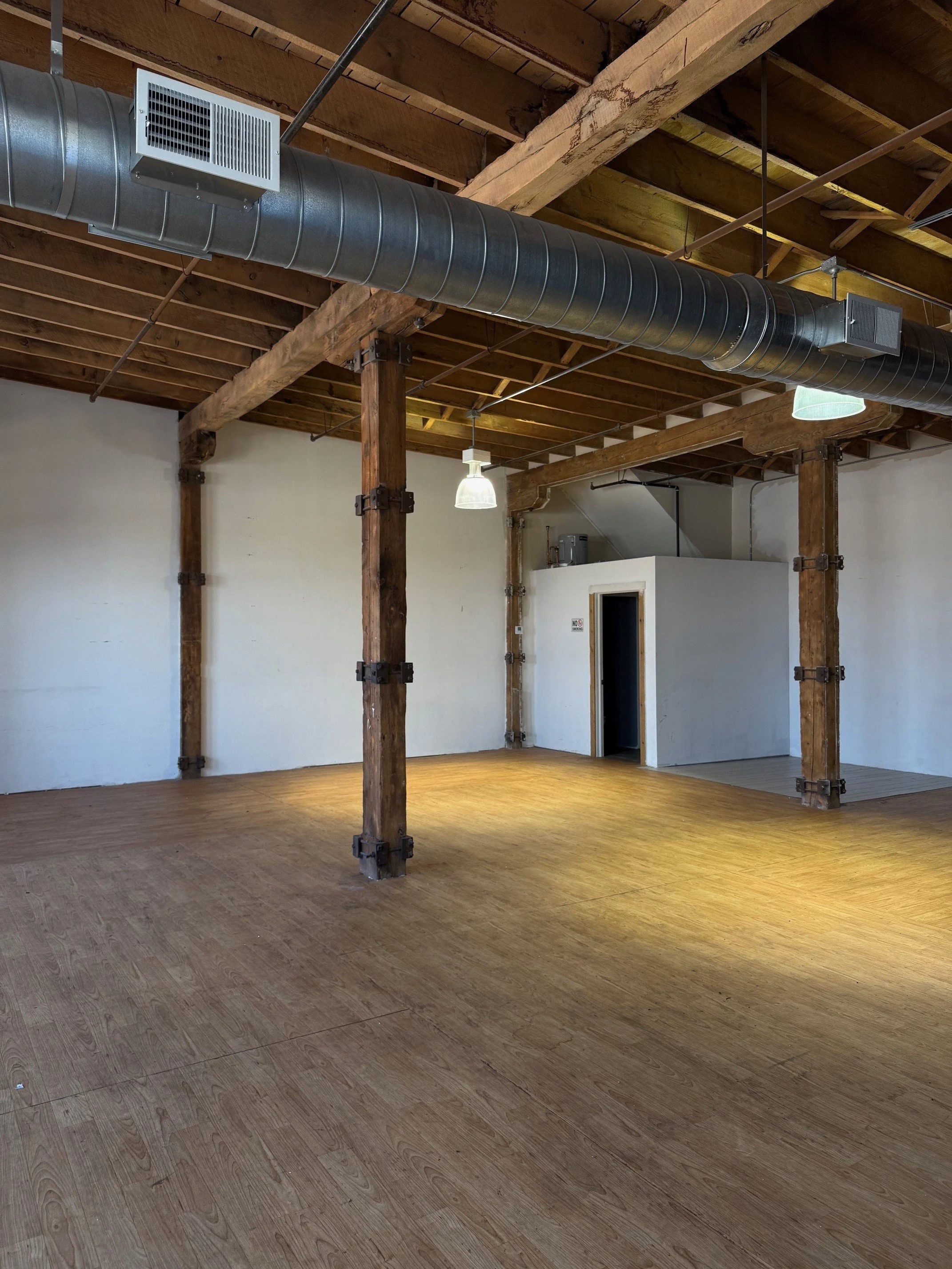 Empty industrial-style room with wooden beams, exposed ductwork, and a small doorway.