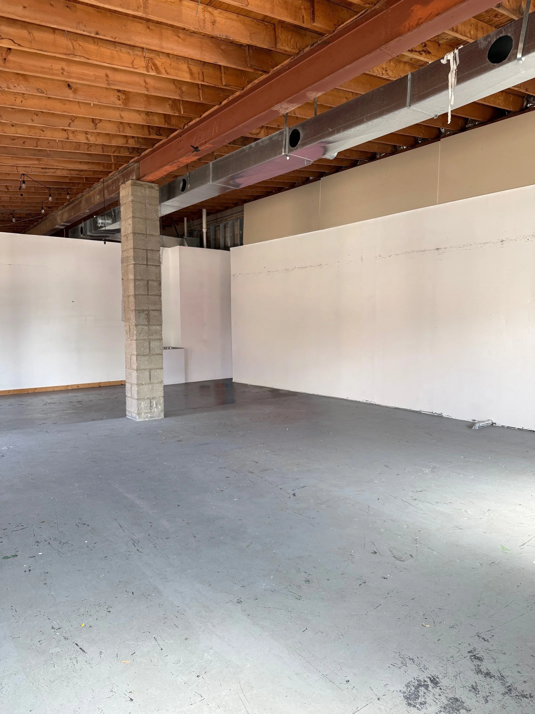Empty interior space with unfinished ceiling, concrete floor, and partial white wall, with an interior support column.