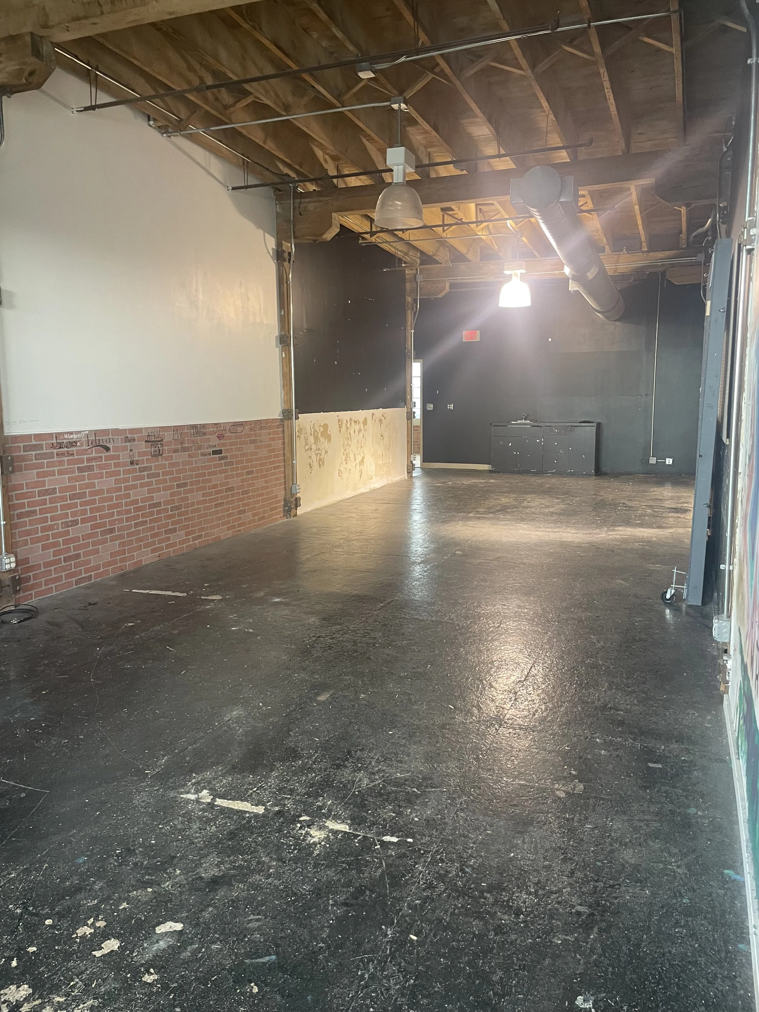 Empty industrial-style room with a wooden ceiling, black and brick walls, black floor, and a few lights hanging from the ceiling.
