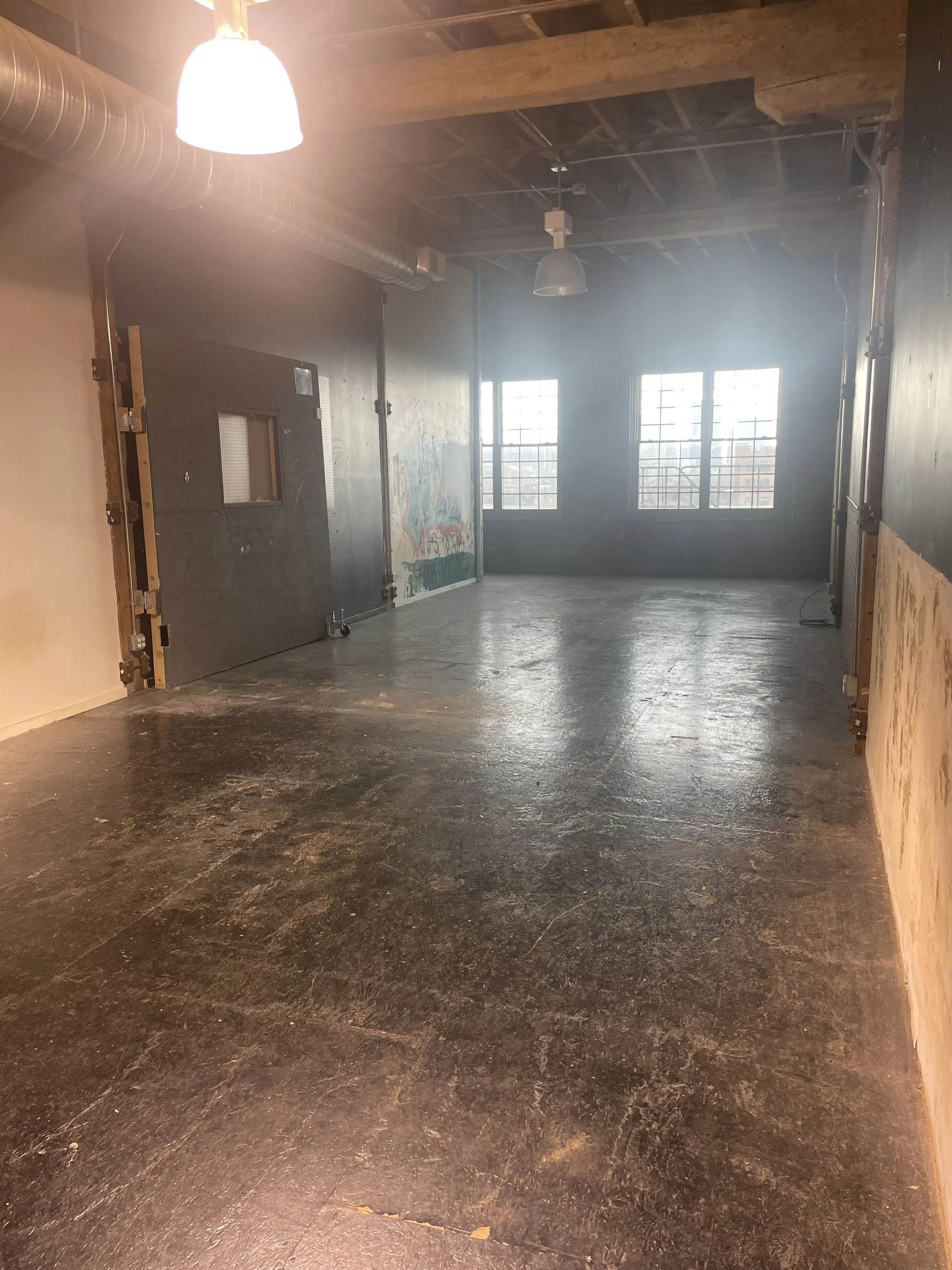 Empty industrial-style room with large windows, wooden ceiling, black floor, and graffiti on the wall.