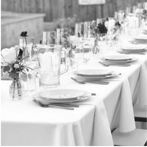Long banquet table set with white tablecloth, plates, glasses, and small floral centerpieces.
