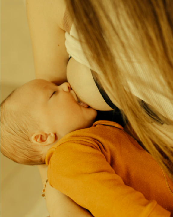 A baby breastfeeding from a woman with long hair, wearing an orange top.