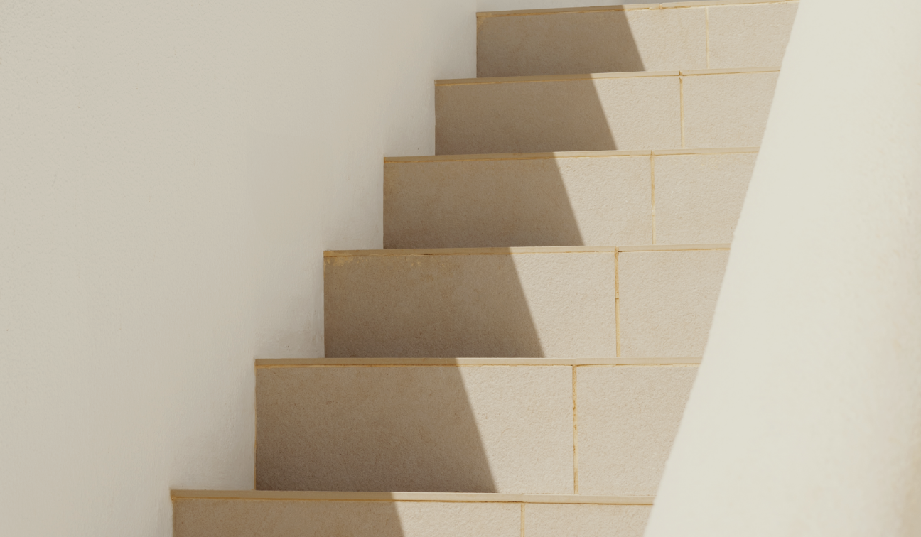 A staircase with beige steps casting shadows on a light-colored wall.