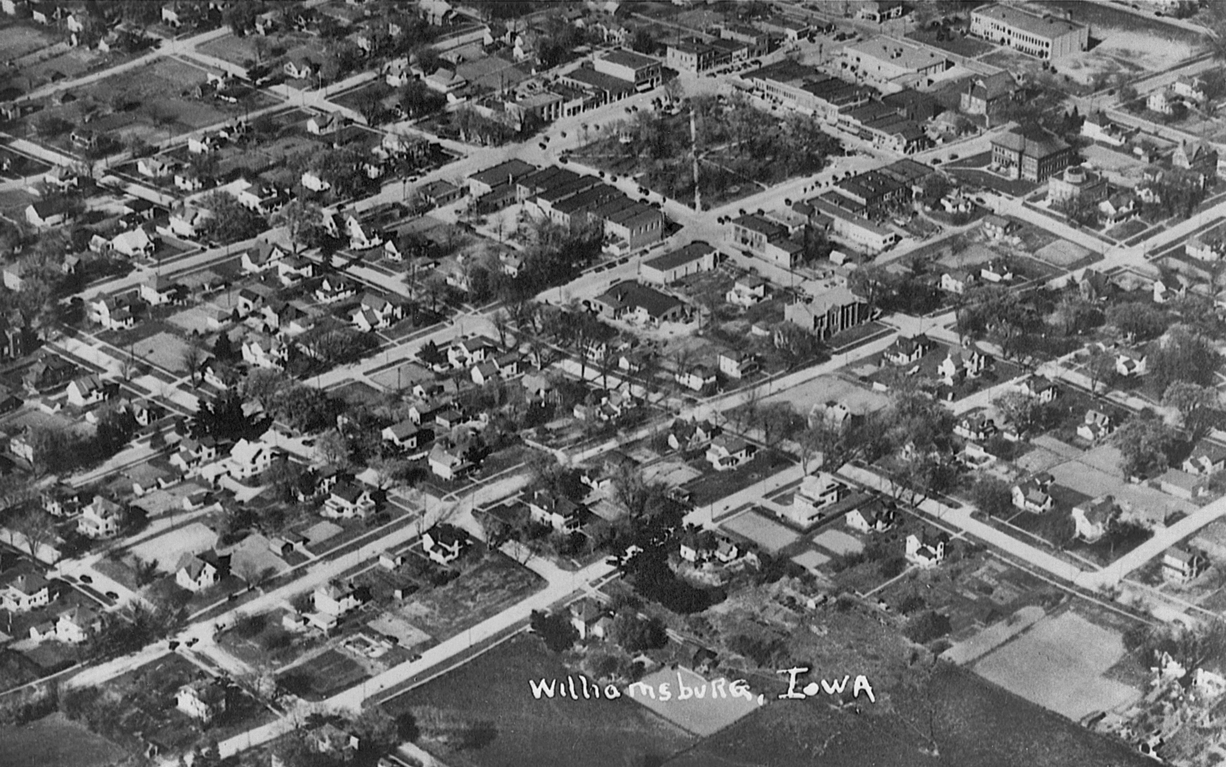 Aerial black and white photograph of a residential neighborhood in Williamsburg, Iowa, featuring houses, trees, and straight streets laid out in a grid pattern.