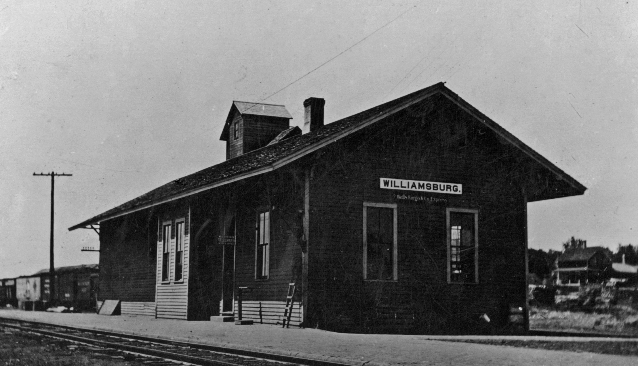 An old black and white photo of the Williamsburg train station with a sign that reads ‘Williamsburg’ and an additional smaller sign beneath it.