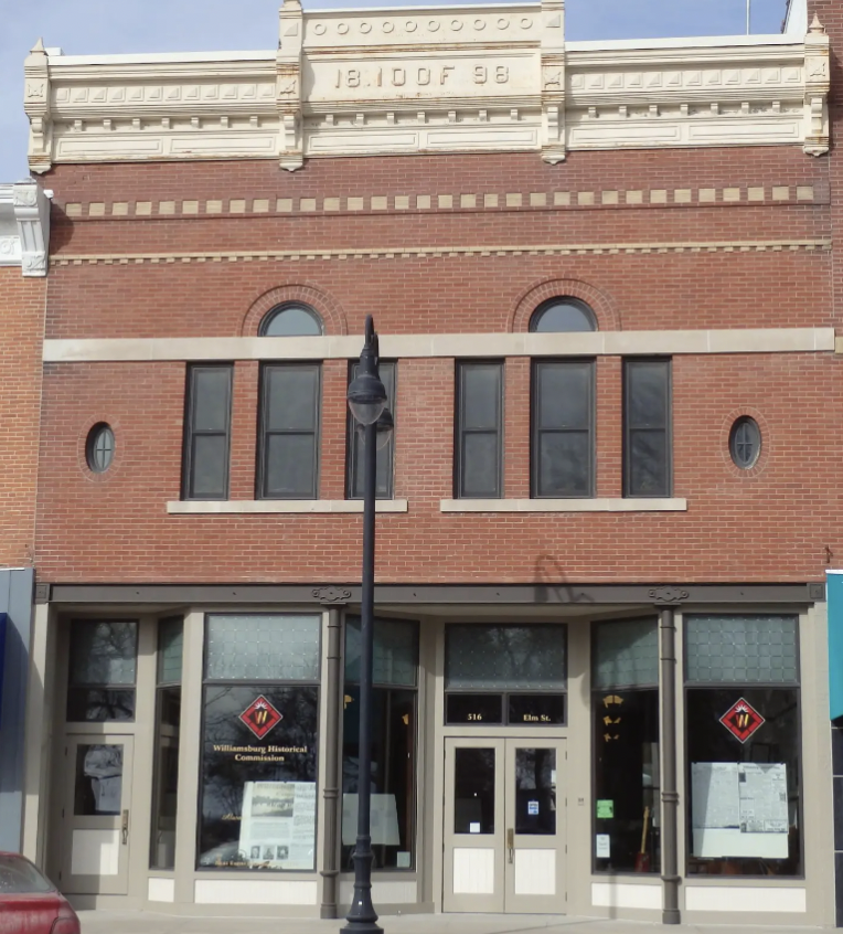 The building has a brick facade with four tall, narrow windows on the second floor, and a sign reading Williamsburg Historical Commission on the door.