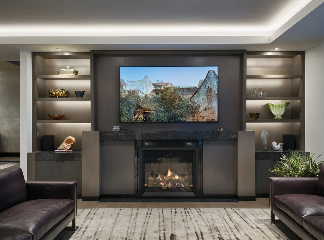 Living room with built-in shelves, a mounted television above a fireplace, and sofas on a beige rug.