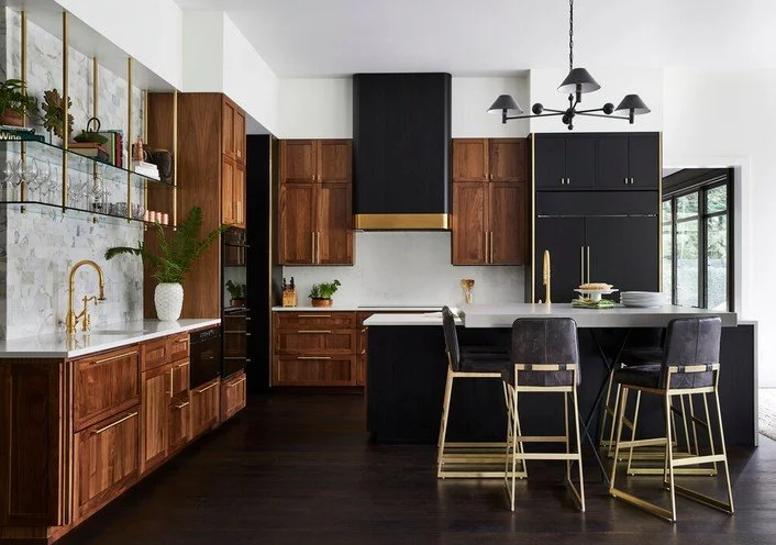 Modern kitchen with wooden cabinets, black accents, gold hardware, and a central island with three bar stools.